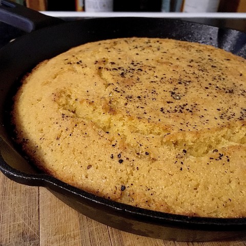 Close up of cornbread baked in a cast iron pan with lovely crisp edges and visible cracking along the top