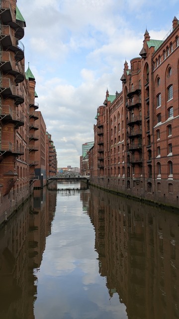 A canal with tall brick warehouses on either side. A bridge