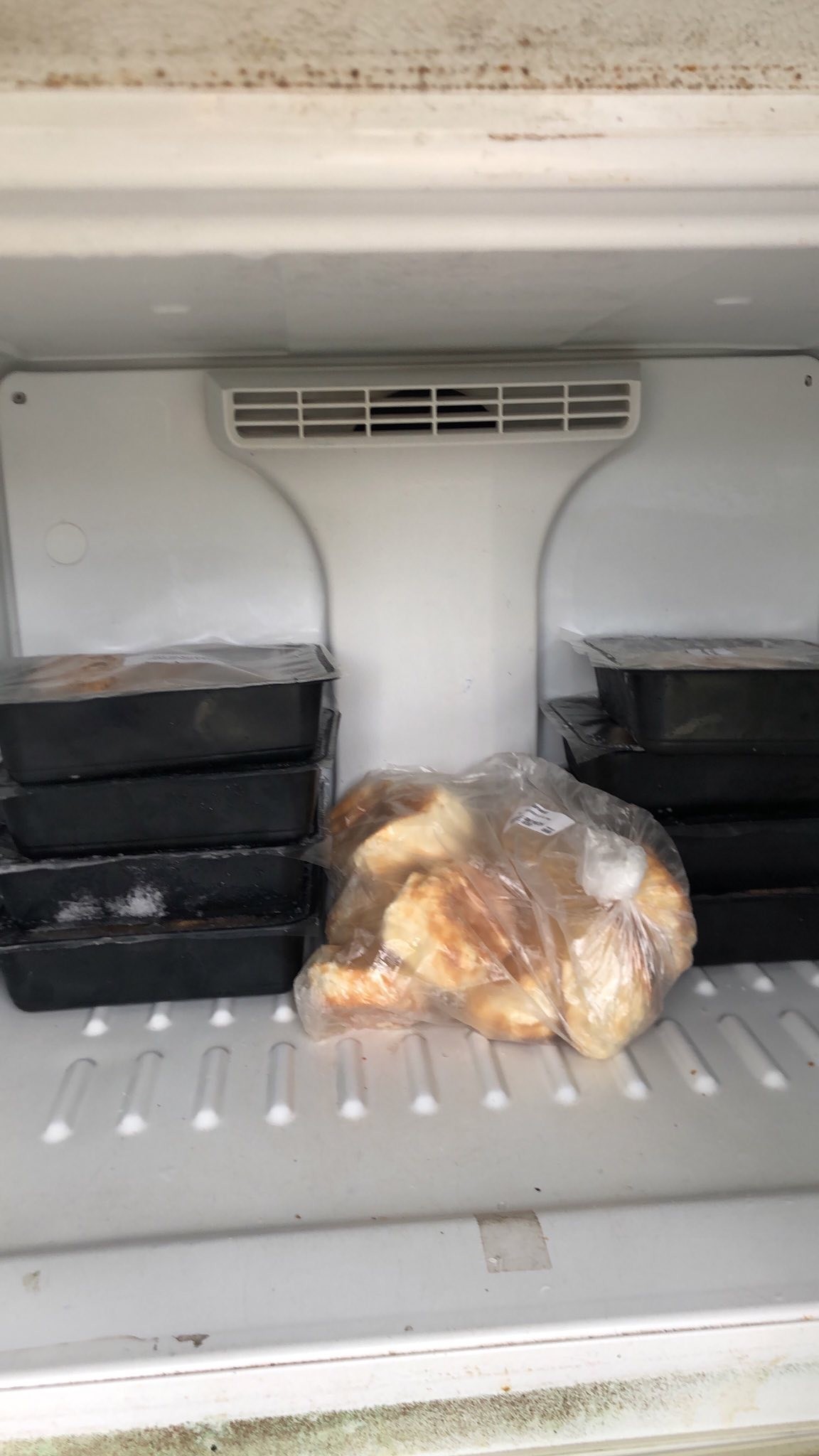 The freezer of the community fridge filled with takeout containers full of kfc fried chicken and a bag of frozen biscuits